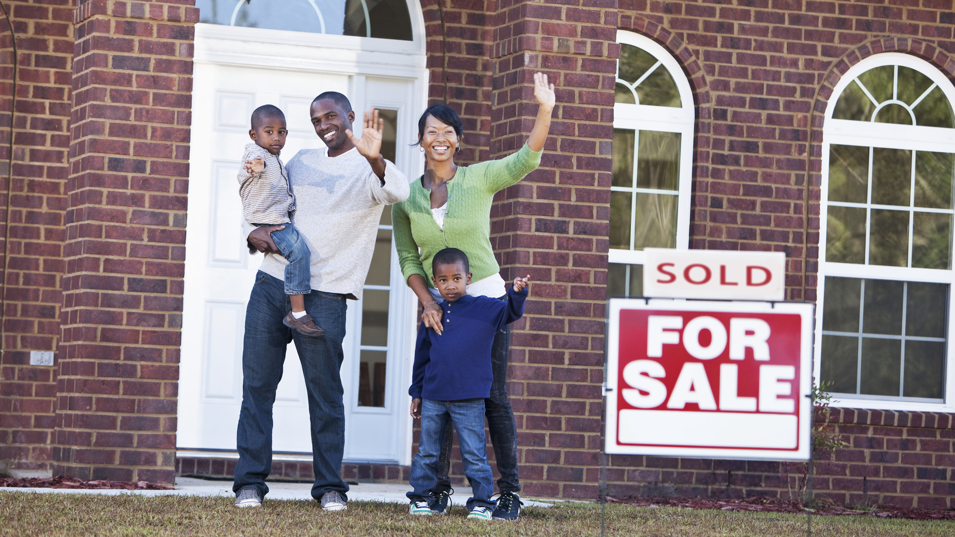 Happy African American family with two young children (4-5 years) waving in front of house with