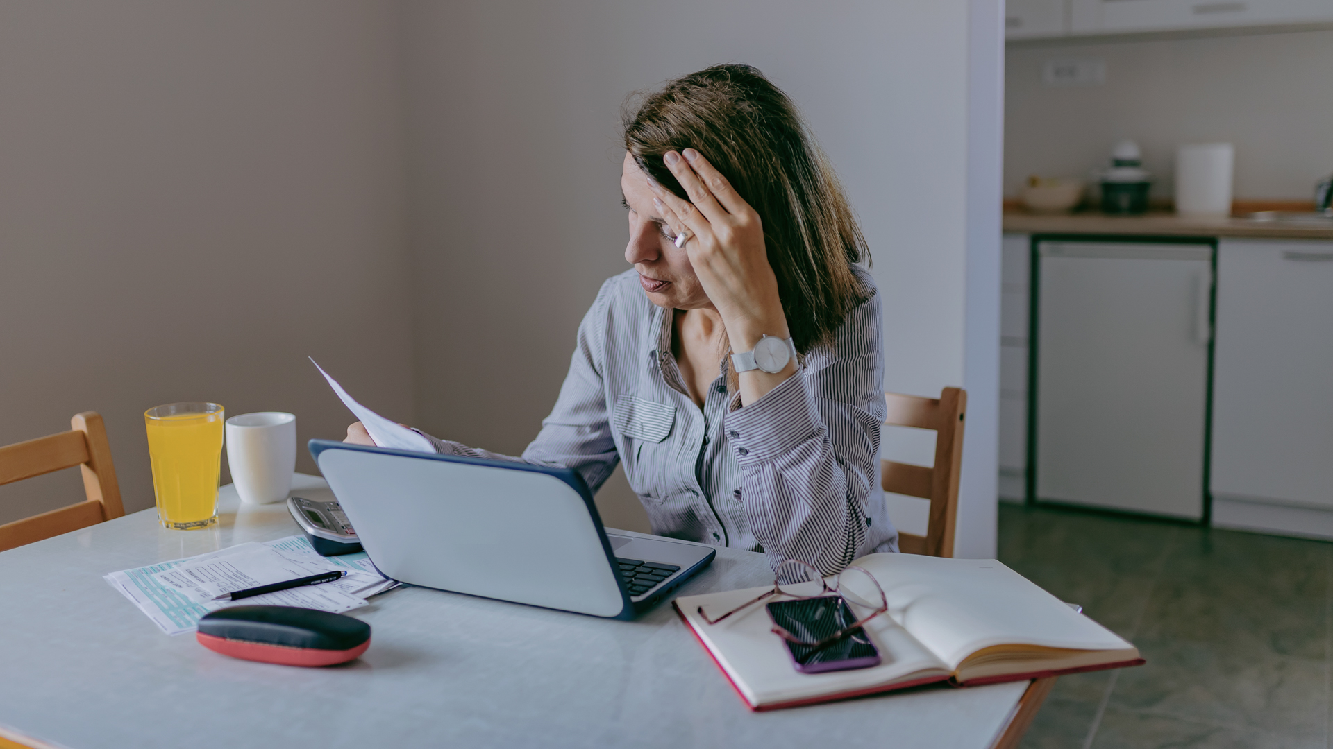 Stressed and Worried Senior Woman Calculating Domestic Expenses, Sitting at Dining Table in Front of Open Laptop Computer.