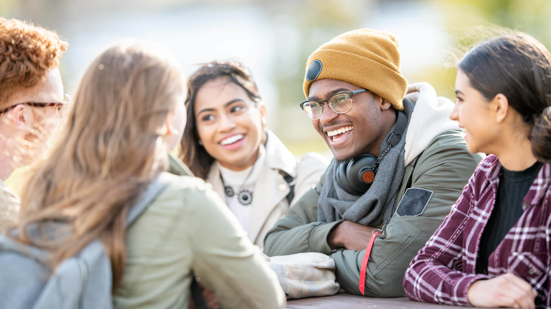 Five young adults are sitting at a picnic table outside on a fall day.